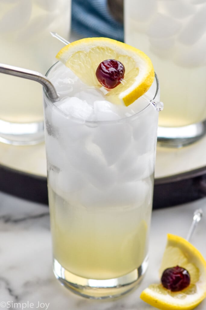 Glass of Tom Collins cocktail with ice, lemon cherry garnish, and straw