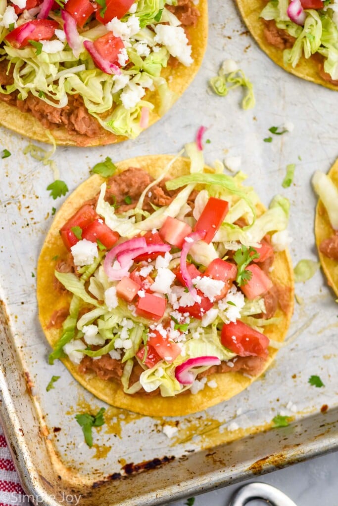 overhead of a toasted with beans, lettuce, cheese, tomatoes, and pickled red onions on a baking sheet