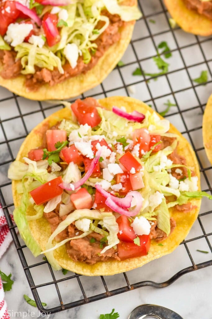 overhead of a tostada with beans, lettuce, tomatoes, cheese on a cooling rack