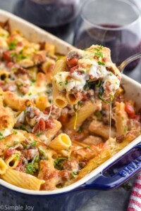 baked rigatoni with sausage being spooned out of a casserole dish