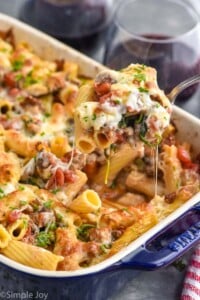 baked rigatoni with sausage being spooned out of a casserole dish