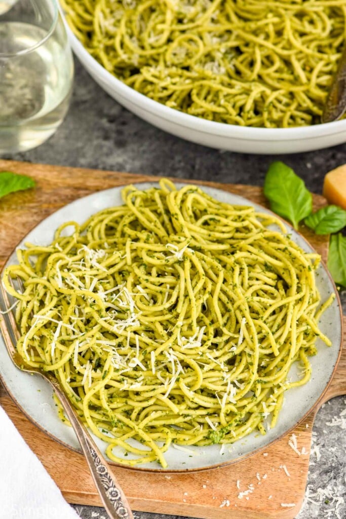 plate of pesto pasta with fork. Bowl of pesto pasta sitting in background.