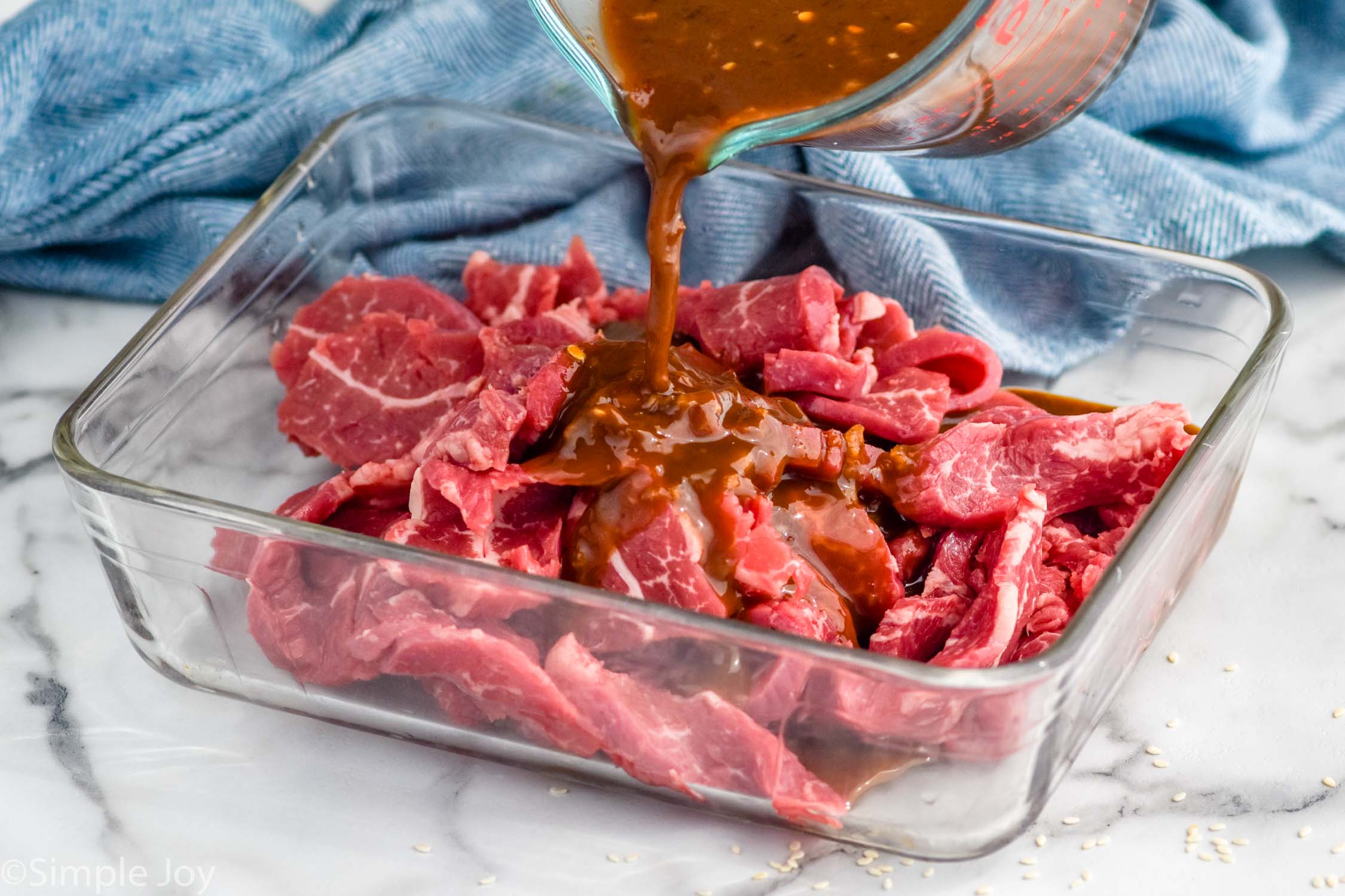 glass measuring cup pouring beef stir fry marinade into a pan of sliced beef to make beef stir fry