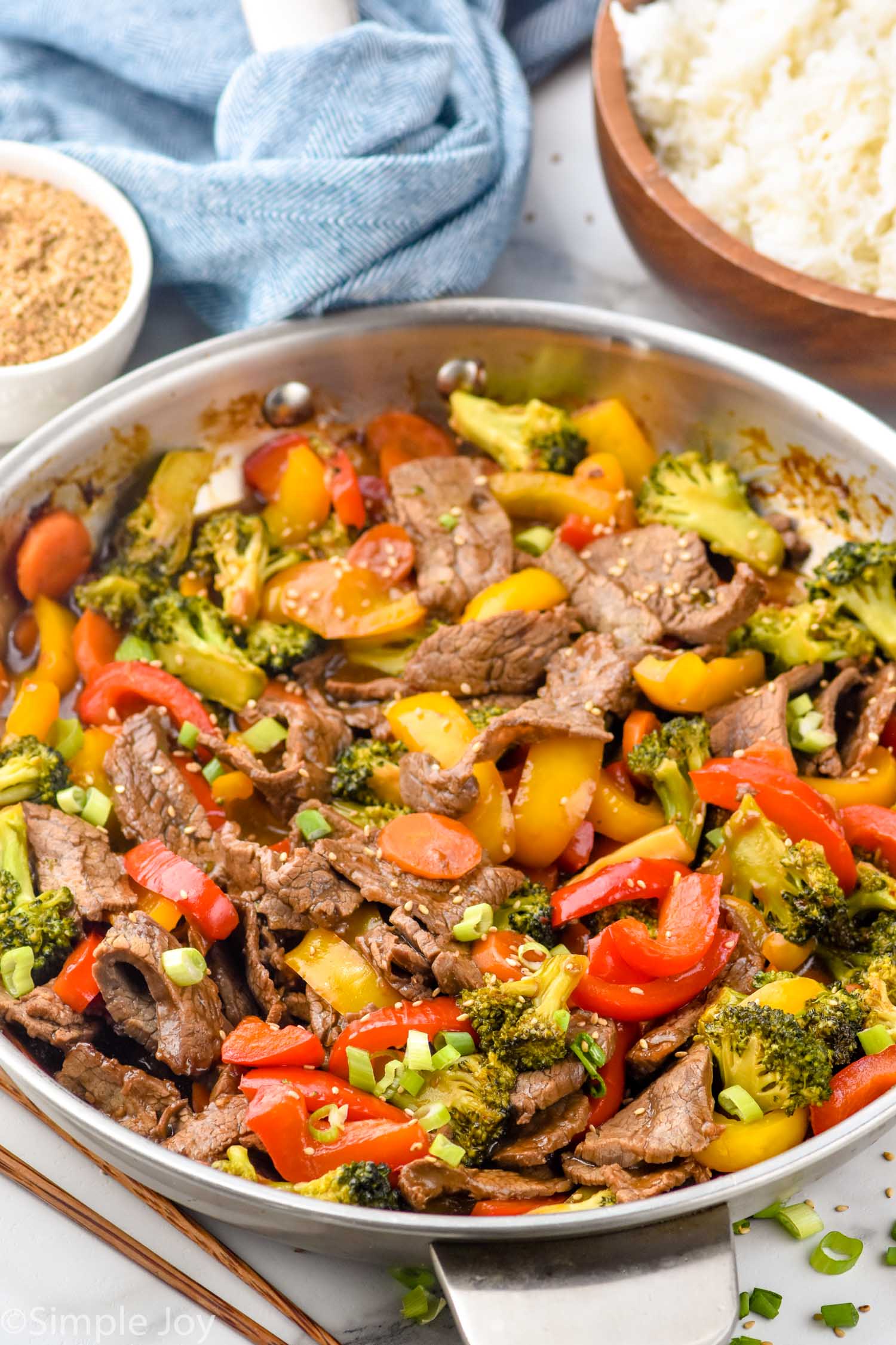Pan of beef stir fry with bowl of white rice and bowl of seasoning sitting in background