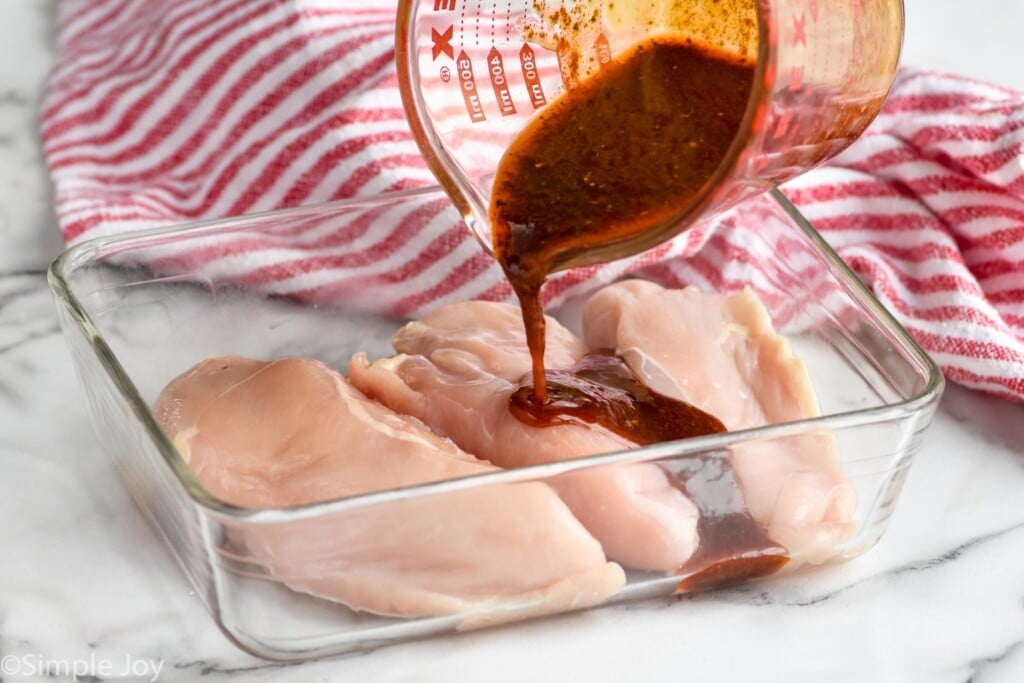 glass measuring cup pouring chicken fajita marinade over chicken breasts to make chicken fajitas