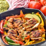 Grill pan of chicken fajitas with lime wedges for serving. Bowl of guacamole and fresh tomatoes sit in background - 12