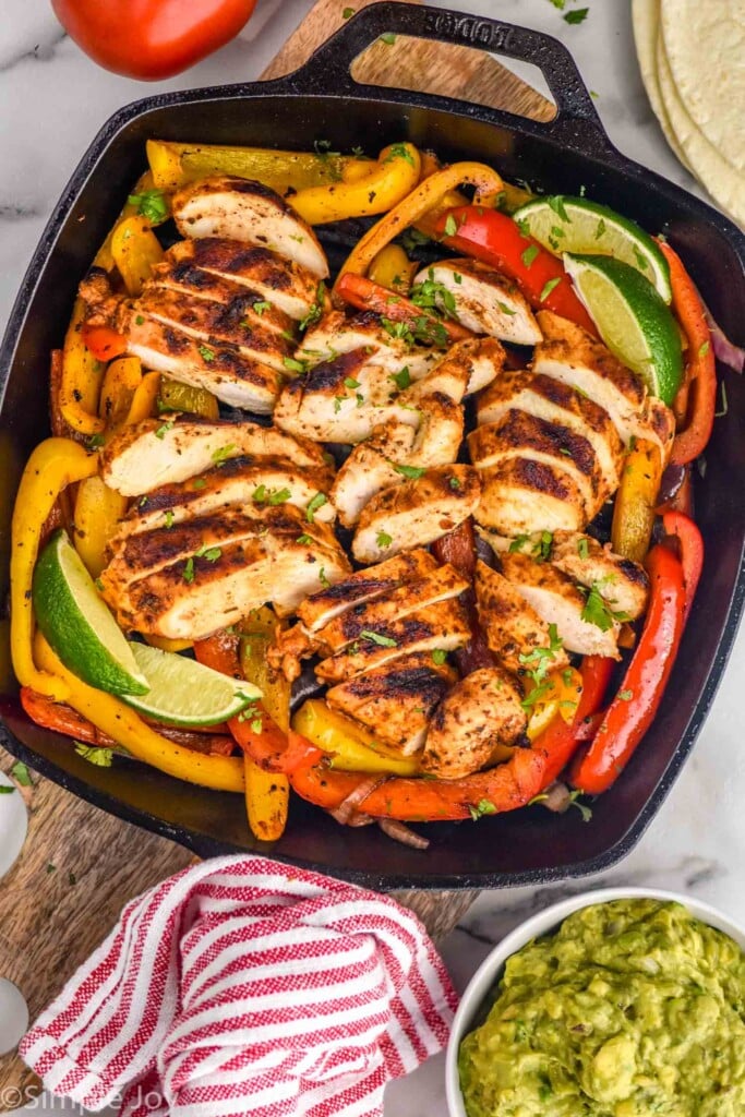 overhead view of grill pan of chicken fajitas with bowl of guacamole sitting beside.