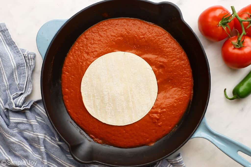 dipping a corn tortilla in enchilada sauce