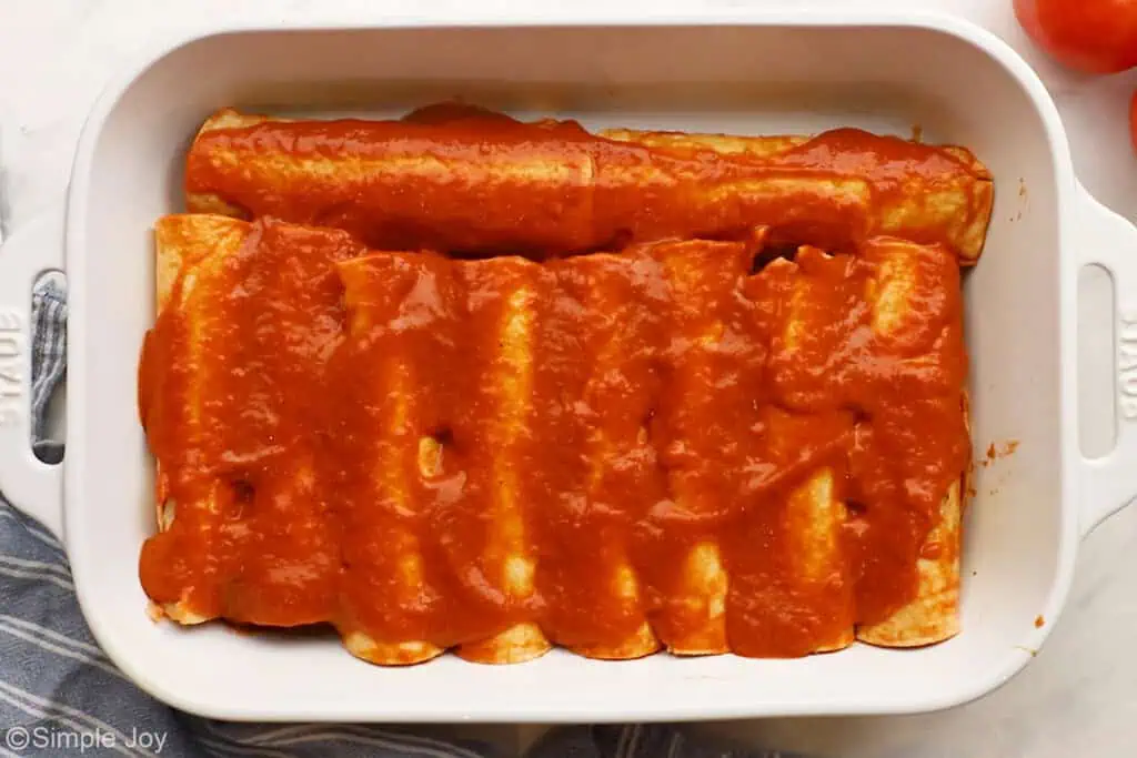 enchilada sauce over unbaked enchiladas in a casserole dish - 12
