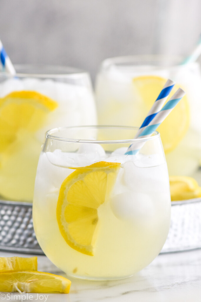 Side view of glasses of Vodka Lemonade garnished with lemon wedges and straws.
