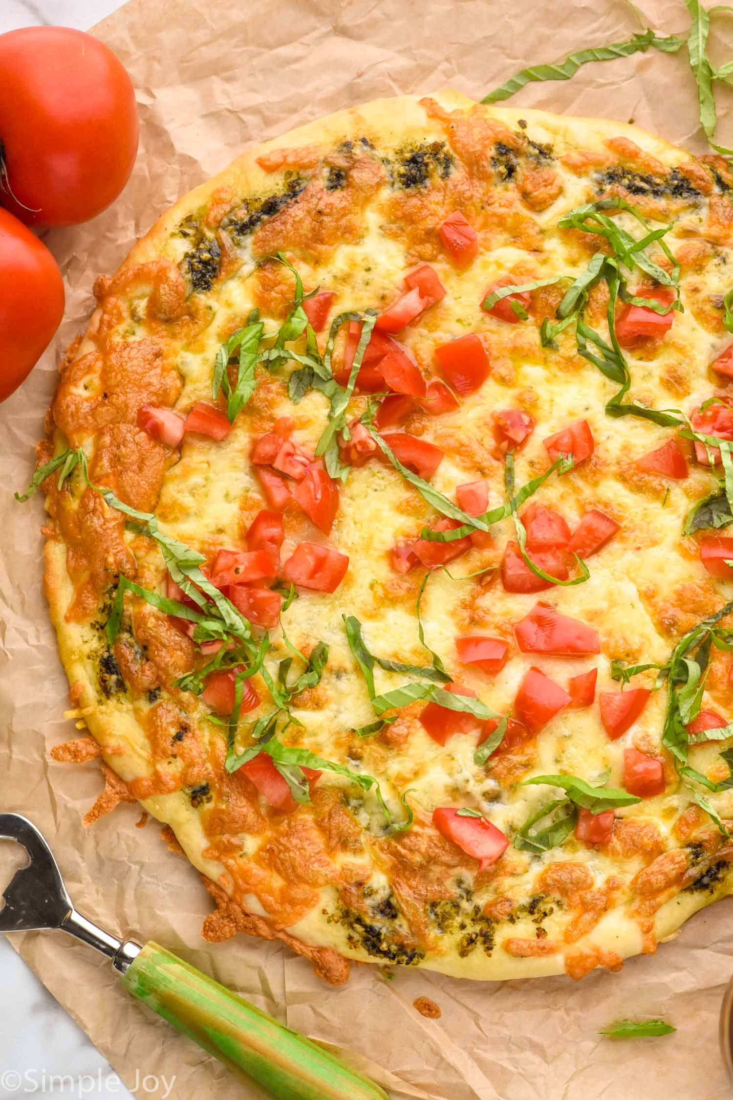 Overhead photo of Pesto Pizza. Tomatoes and bottle opener next to pizza.