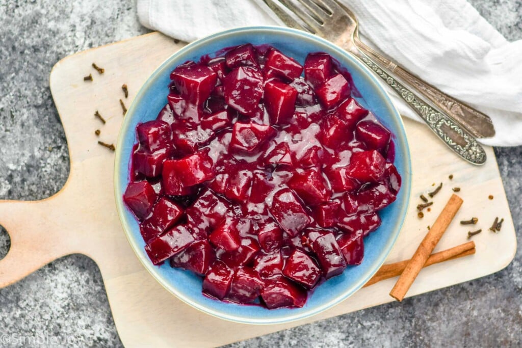 overhead view of bowl of harvard beets with two forks and cinnamon sticks sitting beside