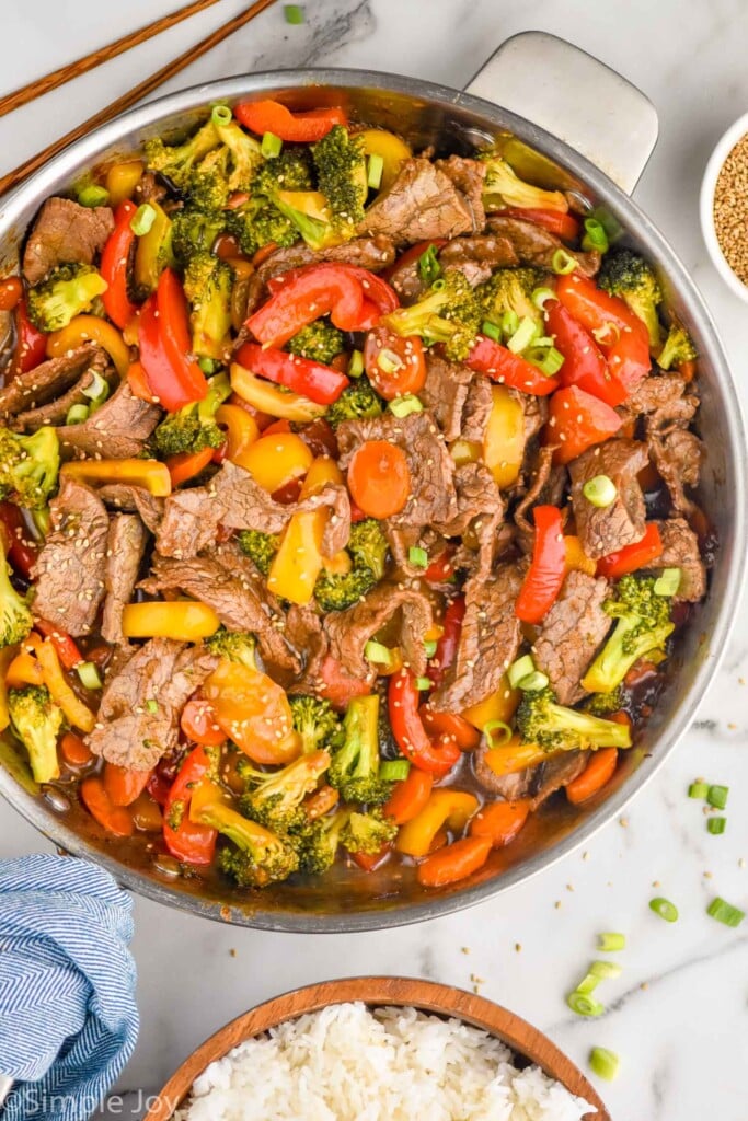 overhead view of pan of beef stir fry. Bowl of white rice and chopsticks sitting beside