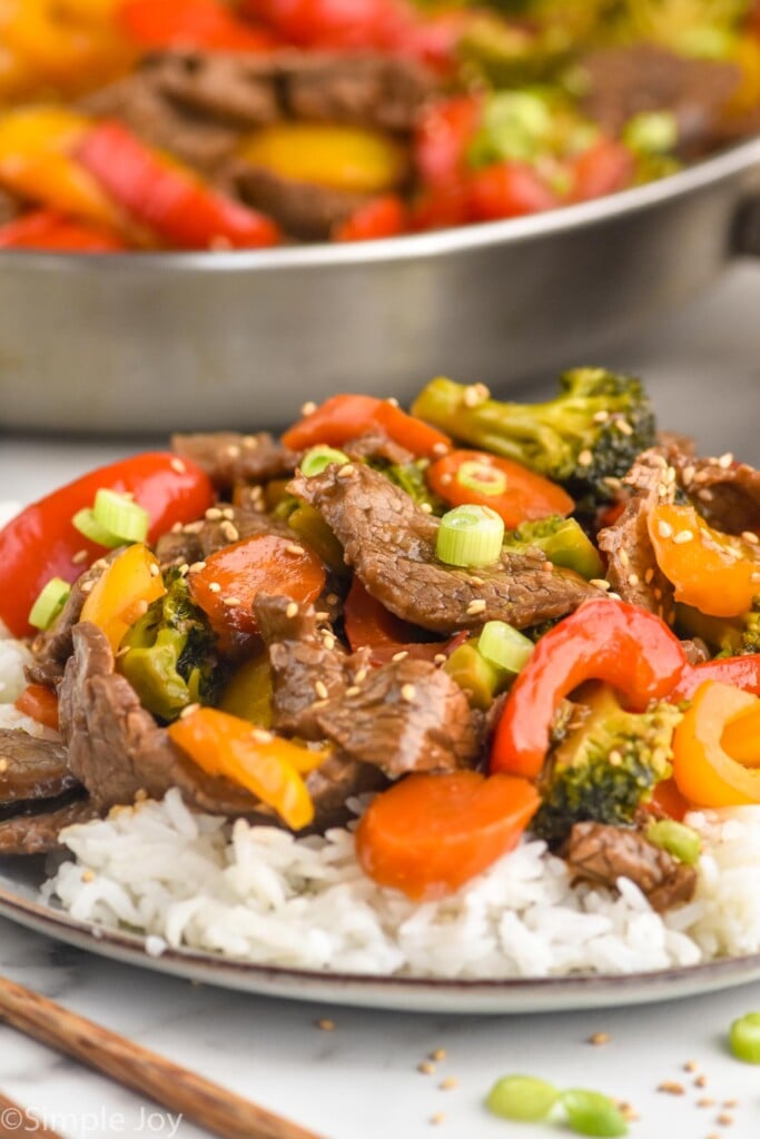 plate of beef stir fry served over rice with pan of beef stir fry sitting in background