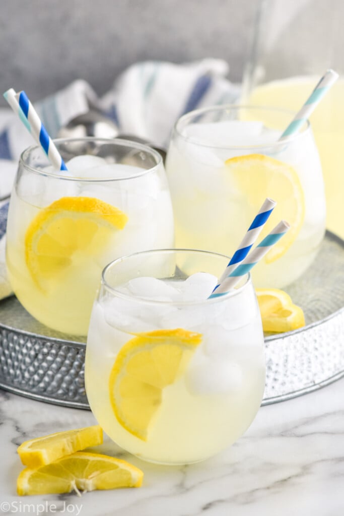 Side view of glasses of Vodka Lemonade garnished with lemon slices and straws. Extra lemon slices beside glasses.