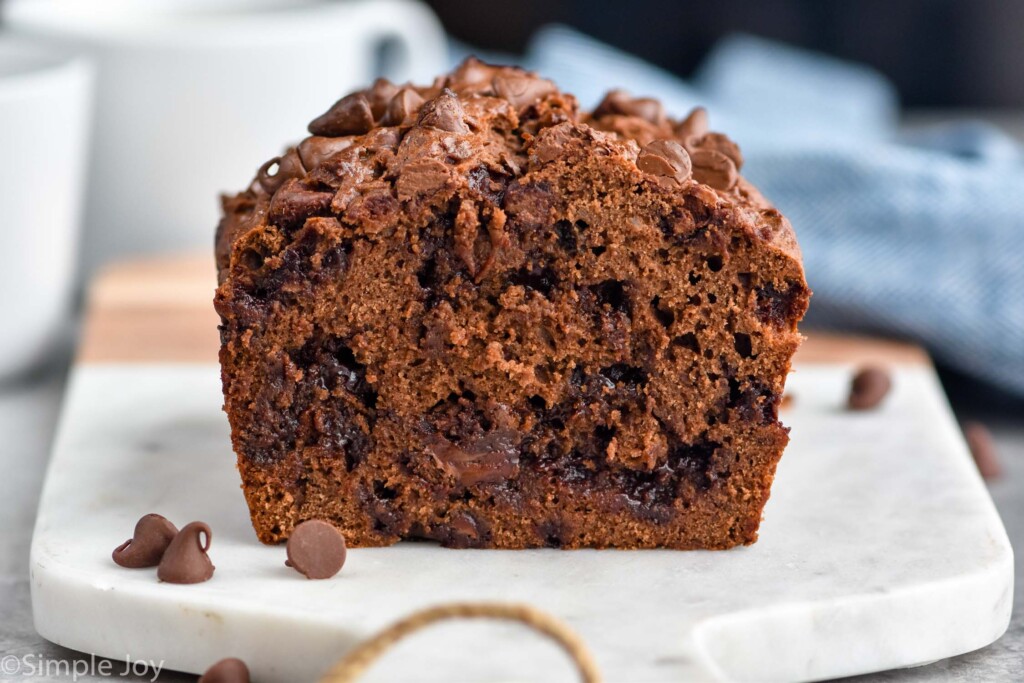 loaf of Chocolate Banana Bread on serving board with chocolate chips sitting beside