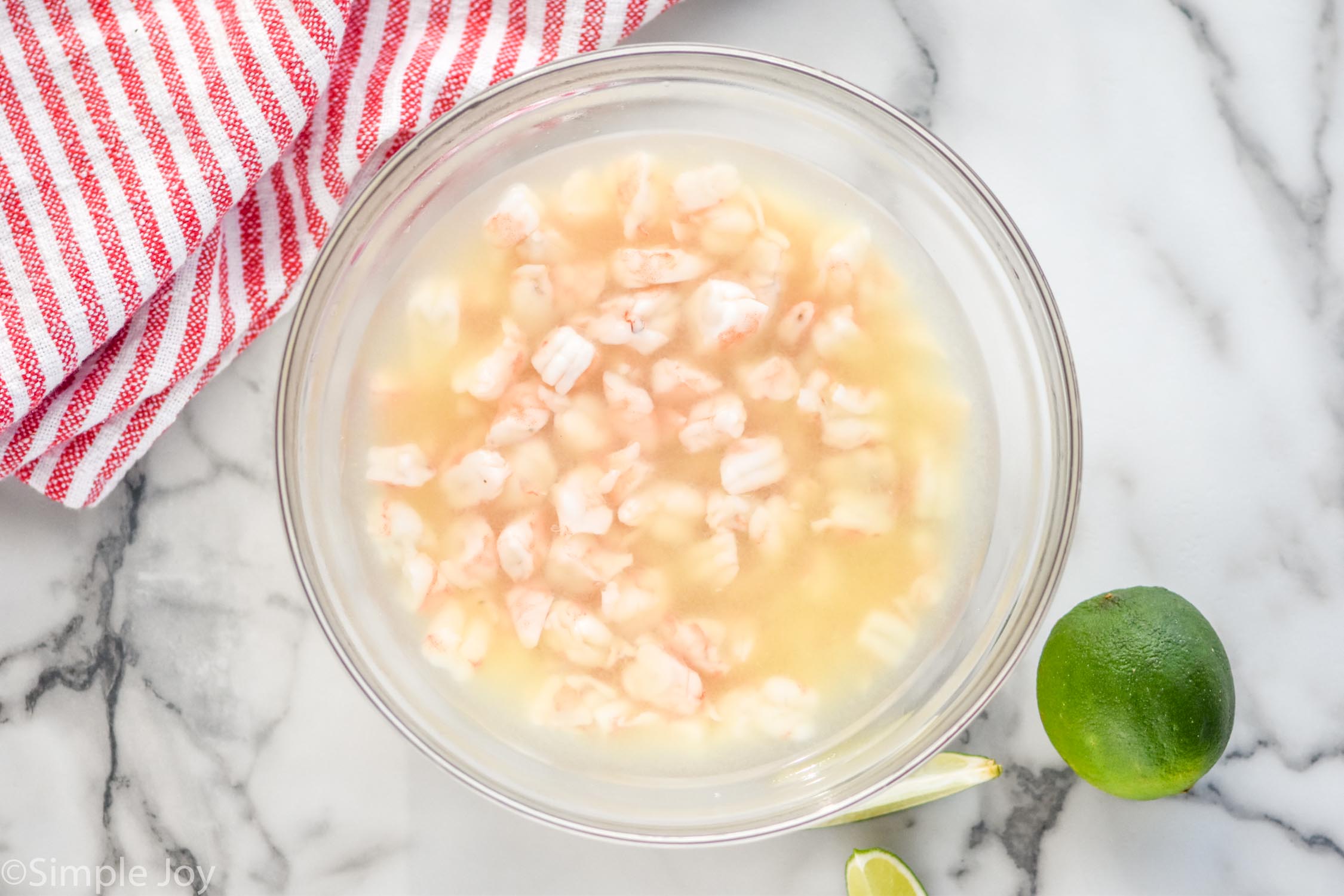 overhead view of a bowl of shrimp in lemon and lime juices to show how to make Shrimp Ceviche. Lime sitting beside bowl.