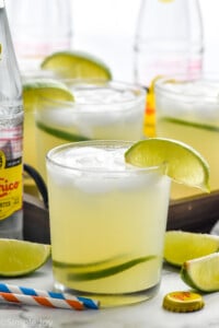 Glass of Ranch Water cocktail with ice and lime wedge. Ranch water ingredients sitting in background