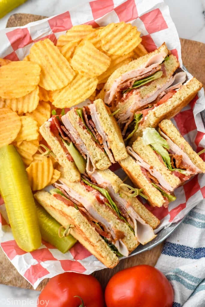 basket with club sandwich, chips, and a pickle spear. Tomatoes sitting beside.