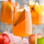 Pinterest graphic for Apple Cider Sangria recipe. Text says, "Amazing Apple Cider Sangria simplejoy.com." Image is side view of glasses of Apple Cider Sangria garnished with apple slices and cinnamon sticks. Extra apples and cinnamon beside glasses.