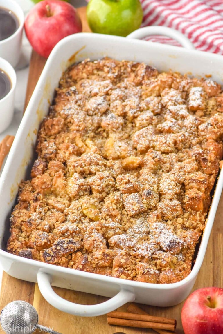 Photo of a baking dish of Apple French Toast Casserole. Apples and cups of coffee beside dish.