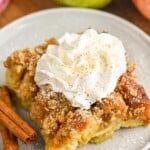 Photo of a piece of Apple French Toast Casserole served on a plate, garnished with whipped cream and cinnamon sticks. Apples beside plate. - 15