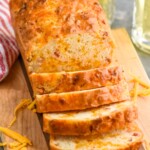 Photo of a partially sliced loaf of Bacon Cheese Beer Bread on a wooden cutting board