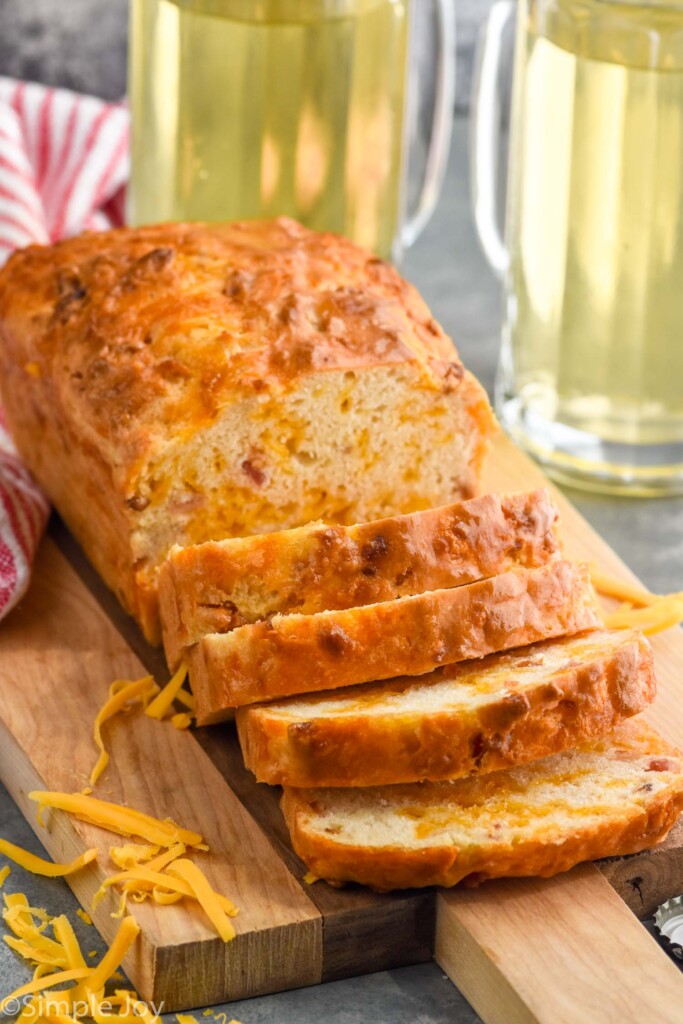 Photo of a partially sliced loaf of Bacon Cheese Beer Bread beside two pitchers of beer