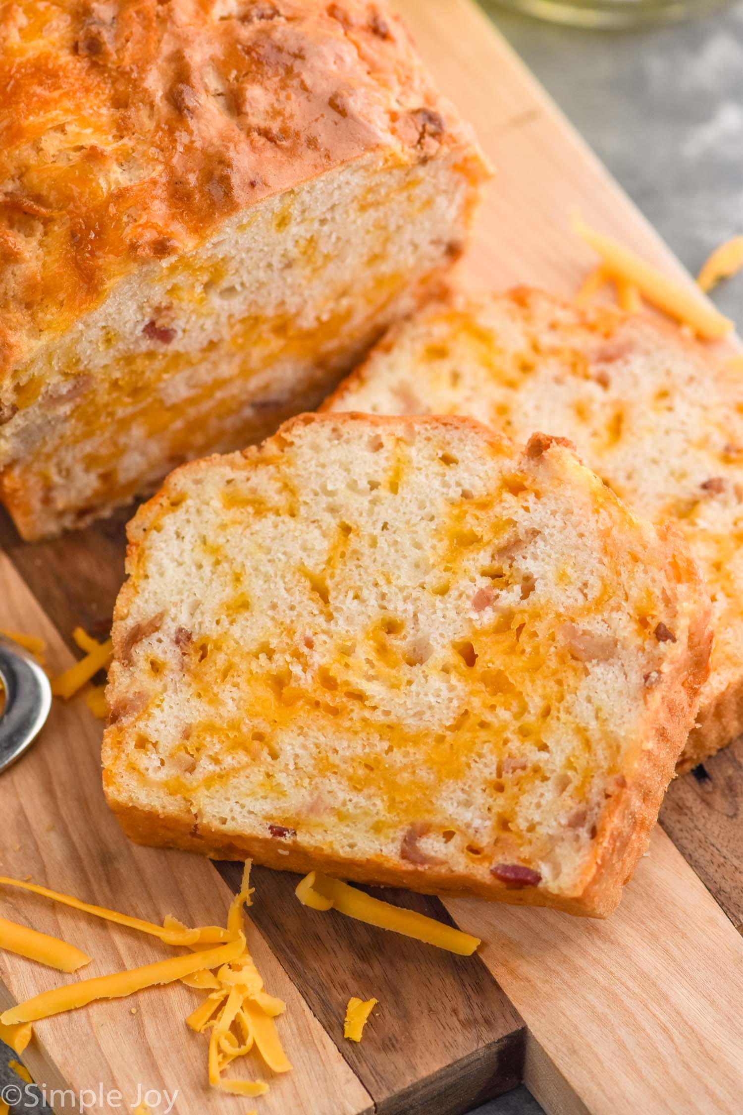 Photo of slices of Bacon Cheese Beer Bread next to the loaf on a wooden cutting board