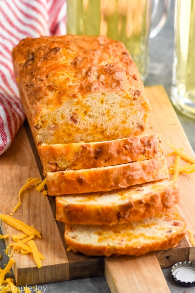 Photo of a partially sliced loaf of Bacon Cheese Beer Bread on a wooden cutting board