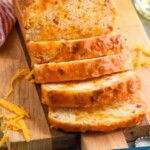 Pinterest graphic for Bacon Cheese Beer Bread recipe. Image shows a partially sliced loaf of Bacon Cheese Beer Bread. Text says, "Bacon Cheese Beer Bread simplejoy.com"