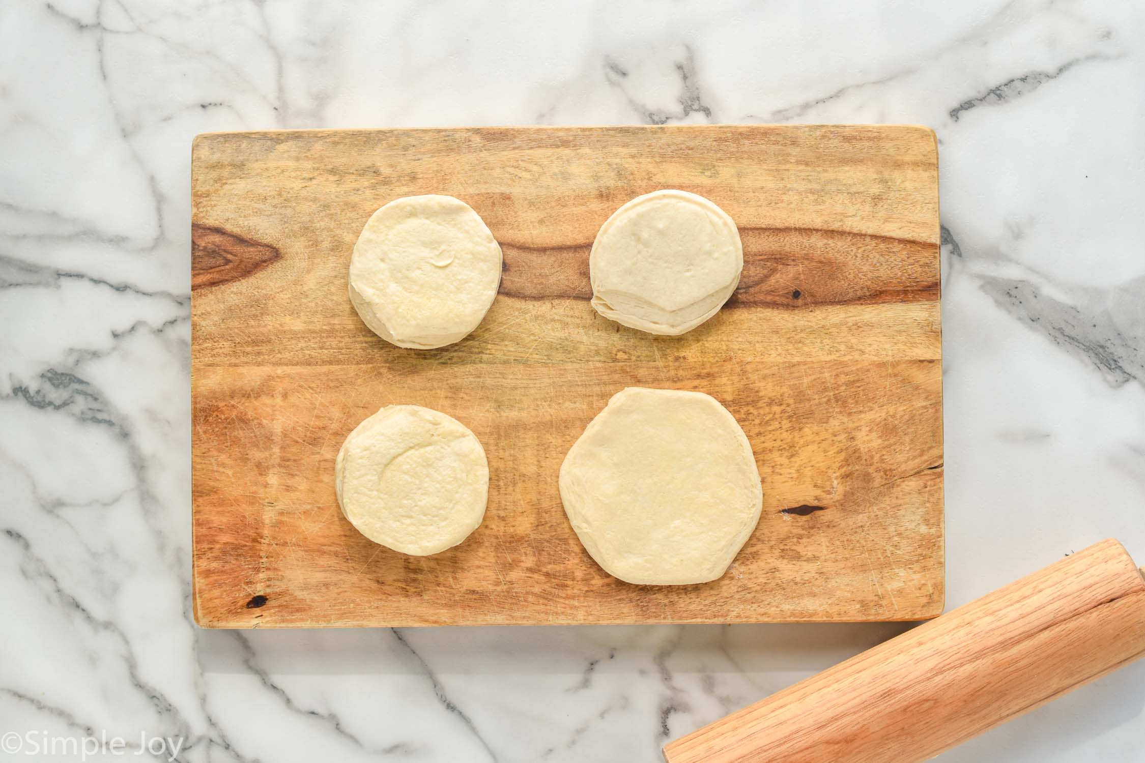 Overhead photo of biscuits on a wooden board with a rolling pin for Mini Calzones recipe.