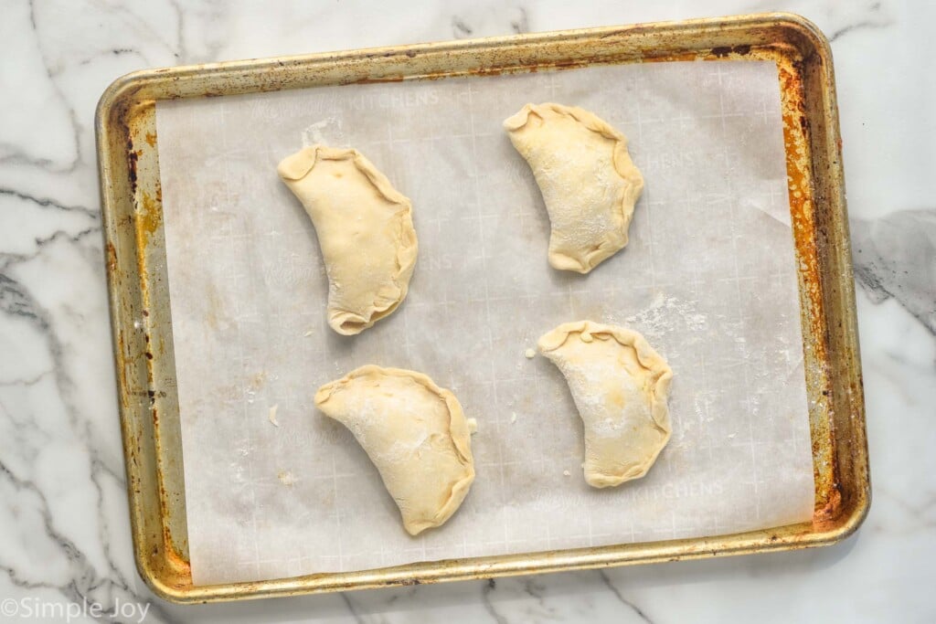 Overhead photo of a baking sheet with Mini Calzones recipe before baking.