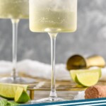 Pinterest graphic for Hugo Spritz recipe. Image is side view of two Hugo Spritz cocktails garnished with lime wedges, with extra lime wedges and cocktail jigger beside wine glasses. Text says, "Hugo Spritz simplejoy.com"