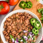 Pinterest graphic for Instant Pot Pinto Beans. Text says "Instant Pot Pinto Beans simplejoy.com" Image shows overhead of bowl of instant pot pinto beans with chopped jalapeno, red onion, and cilantro