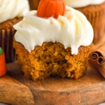Pinterest graphic for Pumpkin Cupcakes recipe. Side view of Pumpkin Cupcakes on a wooden board with a bite taken out of the front cupcake. Text says, "the best Pumpkin Cupcakes simplejoy.com"