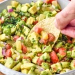 Photo of person's hand dipping chip into bowl of Avocado Salsa