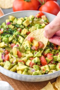 Photo of person's hand dipping chip into bowl of Avocado Salsa