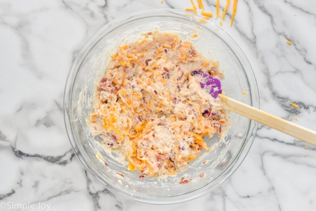 Overhead photo of a mixing bowl of ingredients stirred together with spatula for Bacon Cheese Beer Bread recipe.