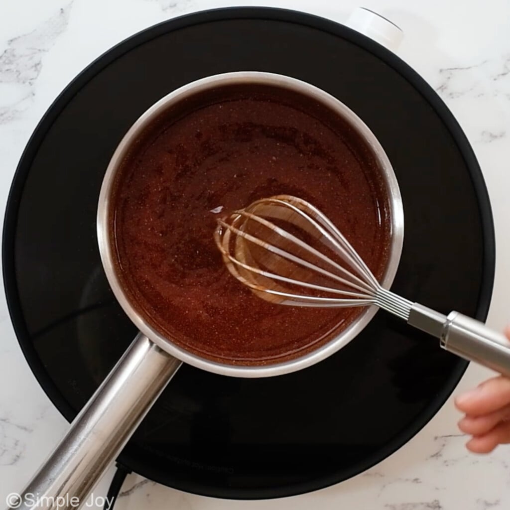 a hand whisking together ingredients for bbq sauce in a small saucepan