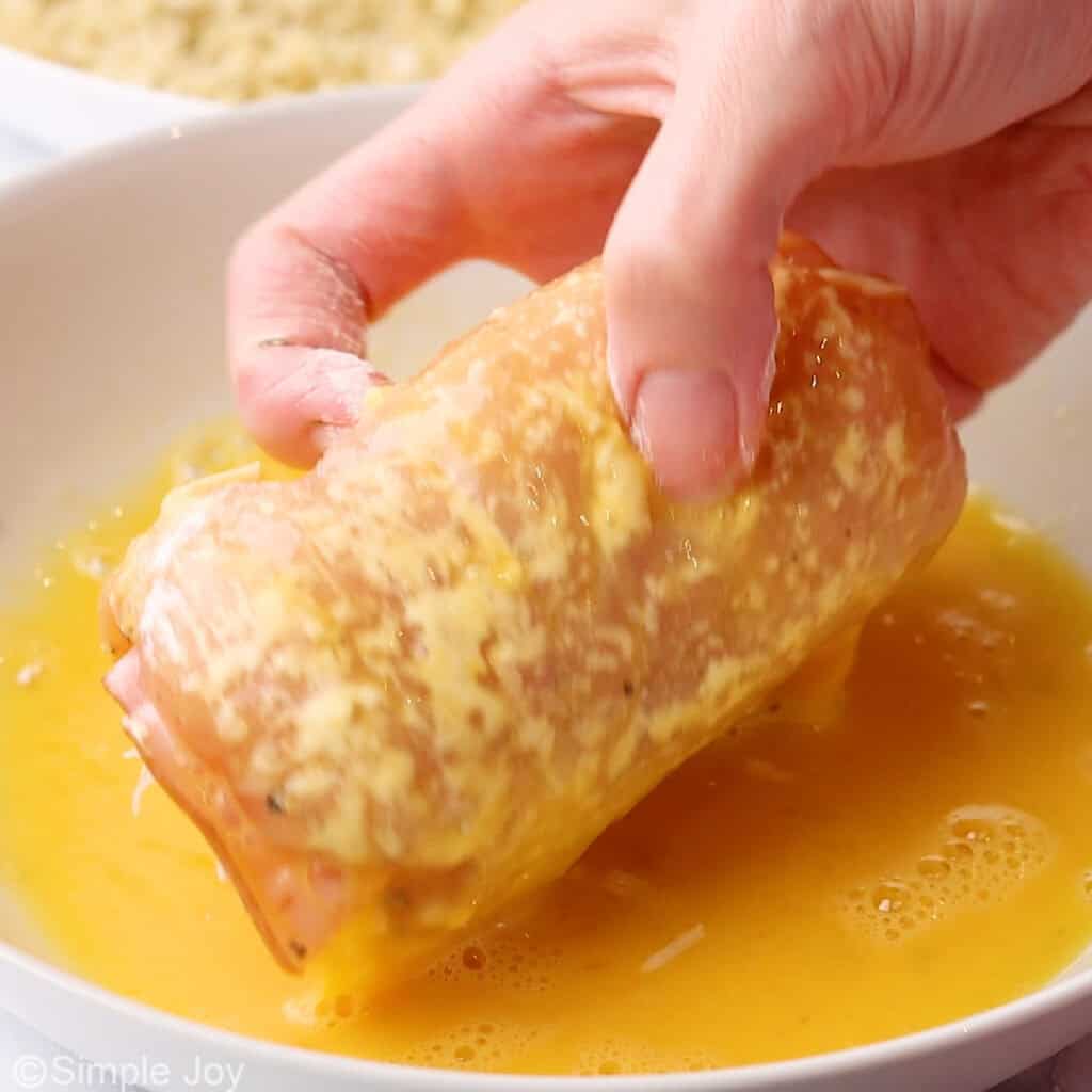 persons hand holding a piece of chicken cordon bleu dipping it in an egg bath