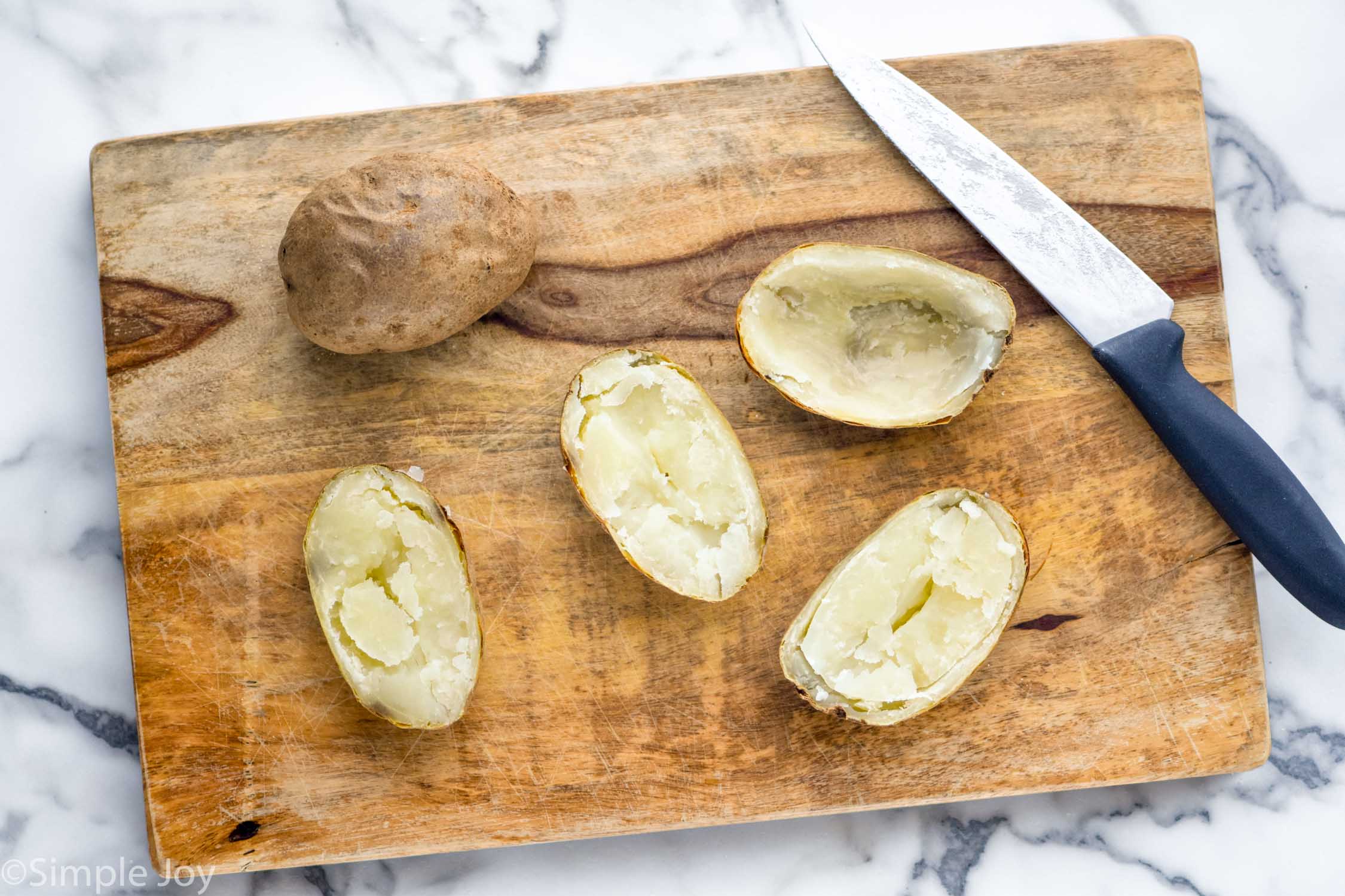 Overhead photo of a cutting board with sliced open potatoes and knife. For Potato Skins recipe.