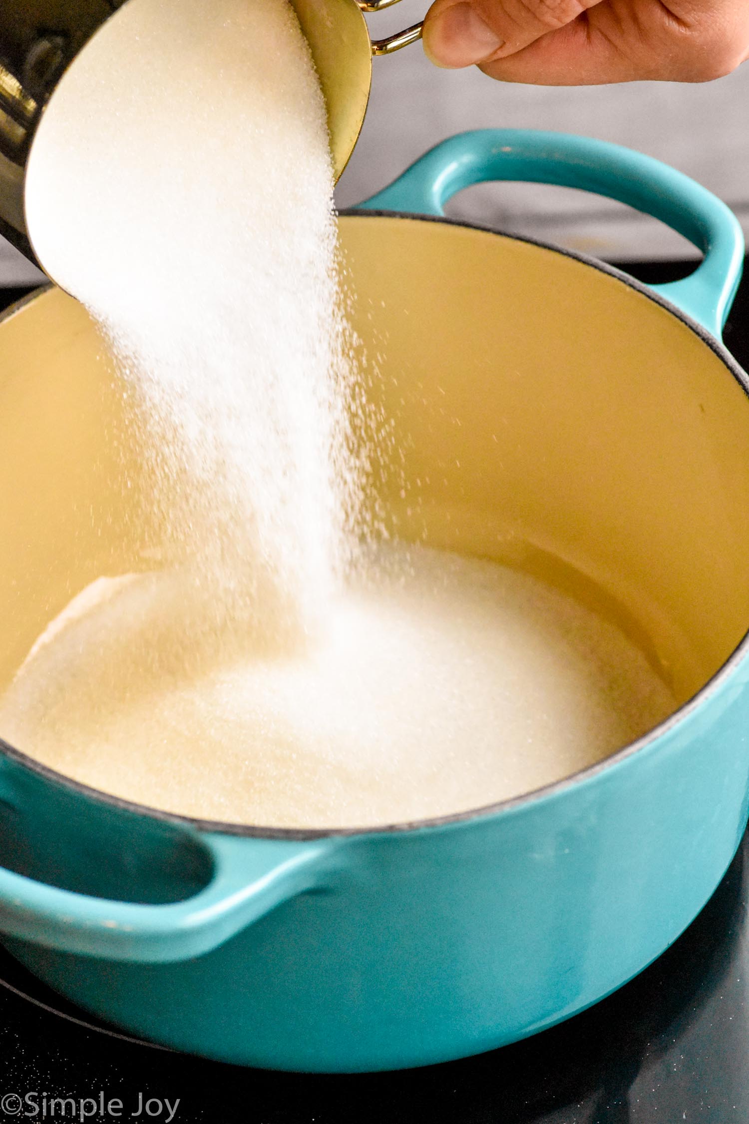 Photo of person's hand pouring measuring cup of sugar into pot for Simple Syrup recipe.