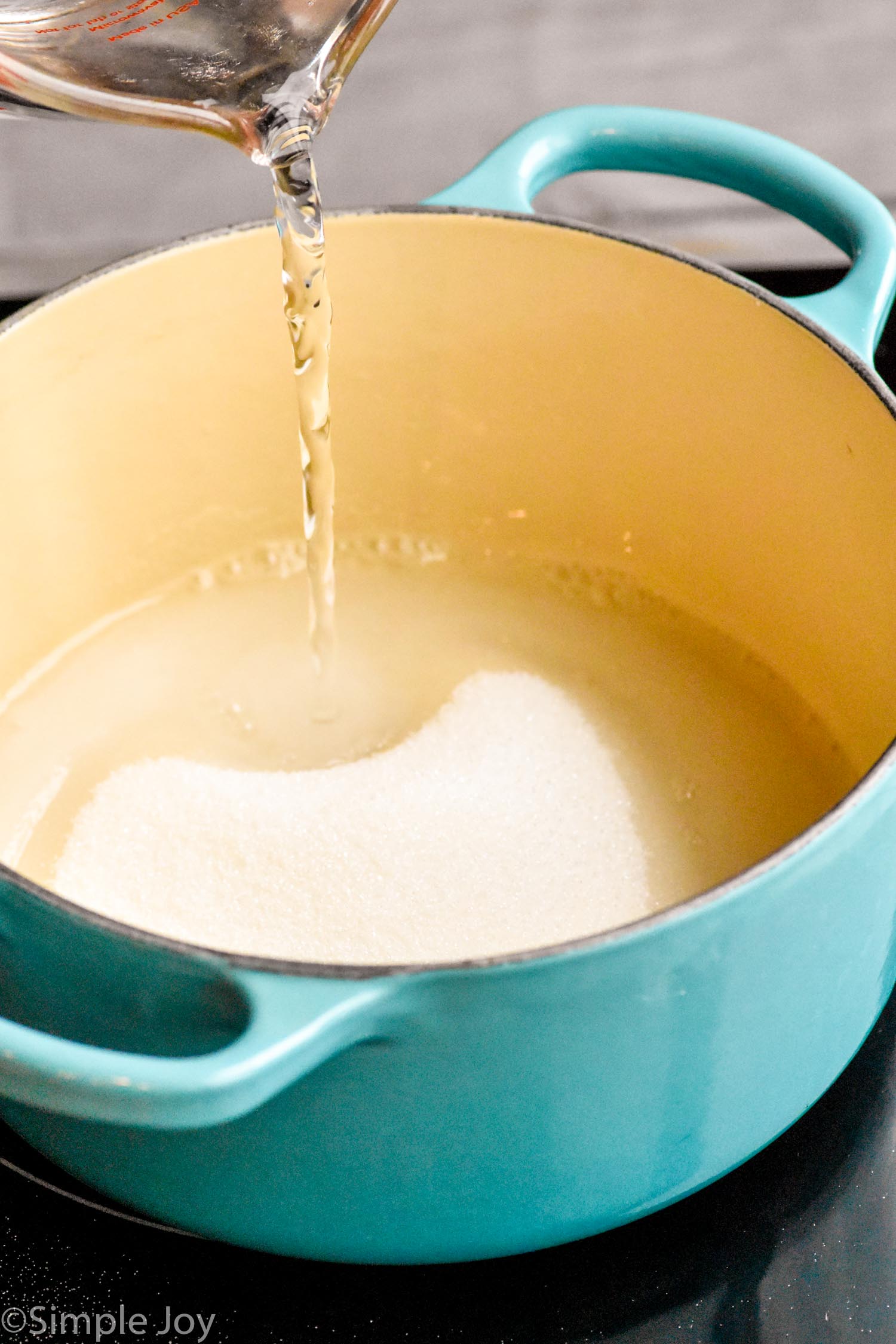 Photo of measuring cup of water being poured into pot of sugar for Simple Syrup recipe.