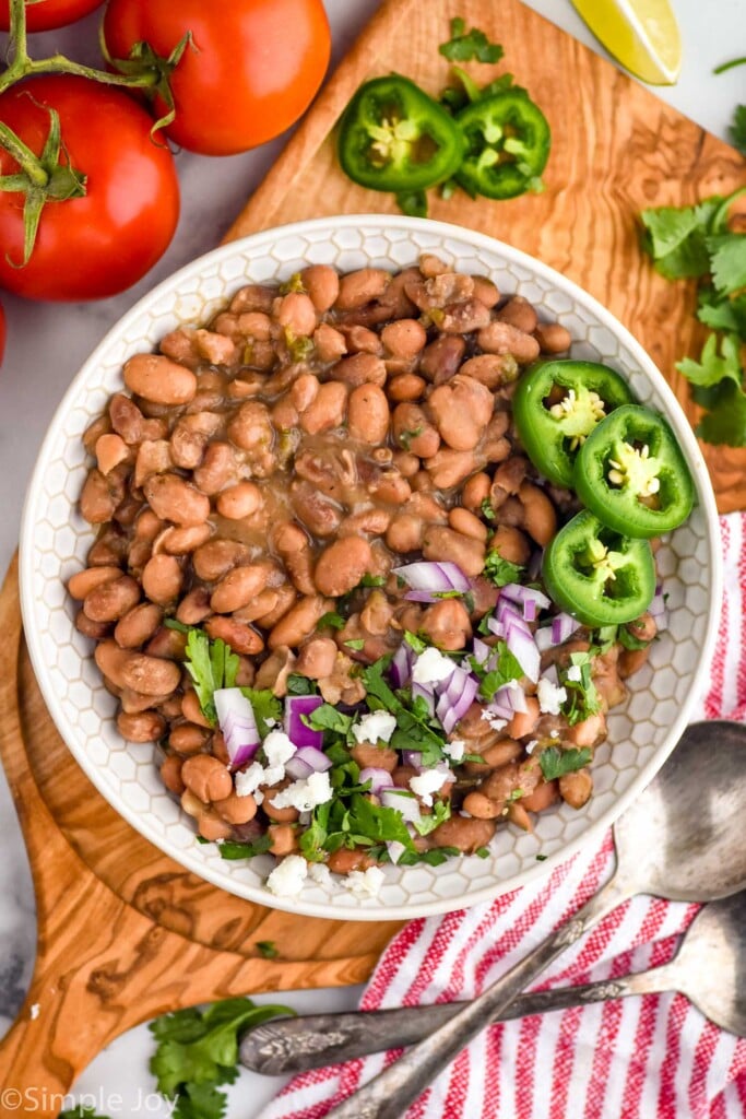 overhead of bowl of instant pot pinto beans topped with cilantro, red onion, diced jalapeno, and lime wedges. vegetables and spoon sitting beside bowl