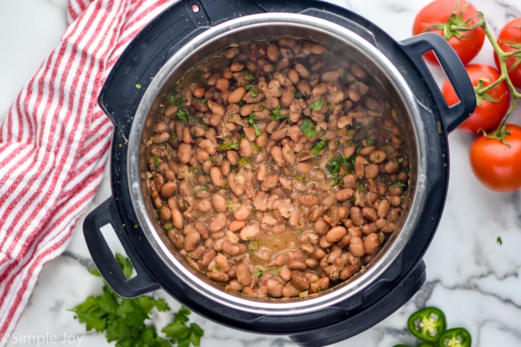 overhead of instant pot with pinto beans. Cilantro, diced jalapeno, and tomatoes sitting beside,