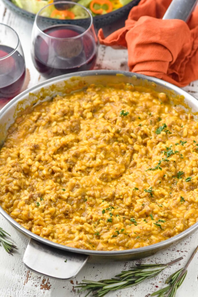 Skillet of Pumpkin Risotto with glass of red wine and bowl of salad sitting in background