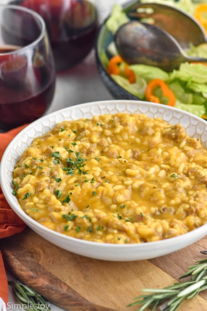 Bowl of Pumpkin Risotto with glass of red wine and bowl of salad sitting in background