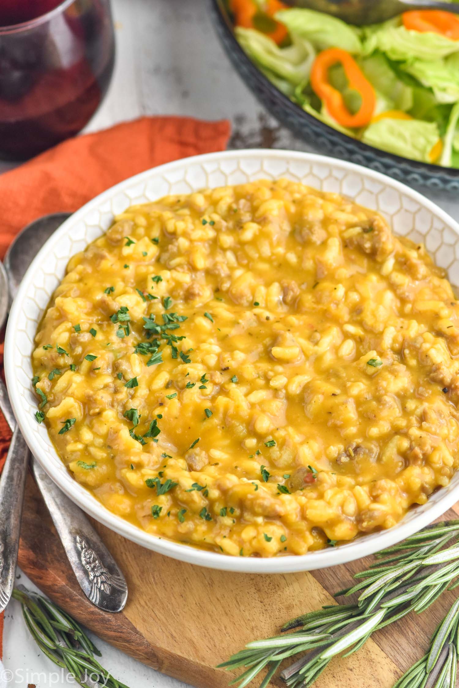 Bowl of Pumpkin Risotto with glass of red wine and bowl of salad sitting in background