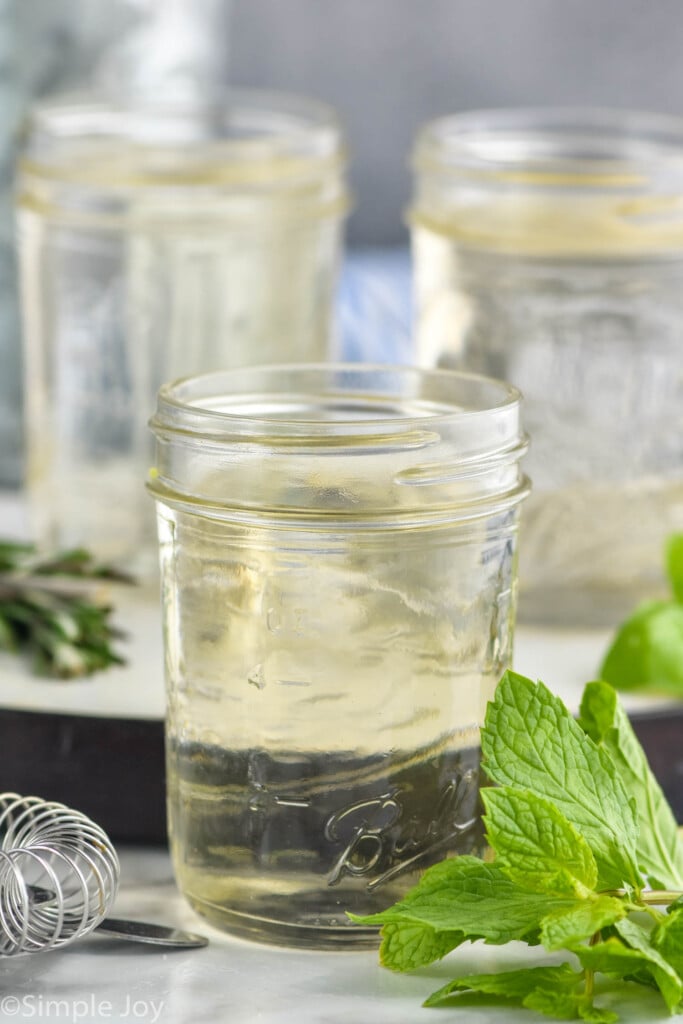 Photo of jars of Simple Syrup next to basil and rosemary leaves.